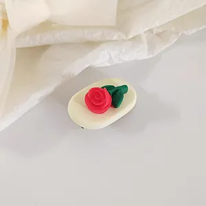 Close-up of a 3D red rose tulip hair clip with green leaves on white textured fabric