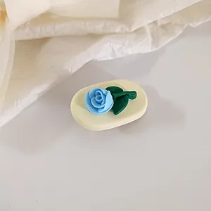 Detailed macro view of a 3D blue tulip hair clip with green leaves on cream base