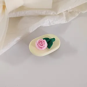Detailed view of a 3D pink rose resin charm with green leaves on a soft yellow base