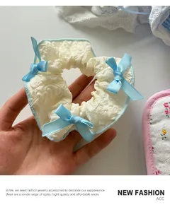 Detail of white jacquard fabric scrunchie with blue satin bow and floral lace detail