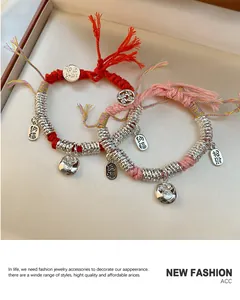 Detailweergave van rode en roze gevlochten armbanden met zilveren gelukshangers op fluweel