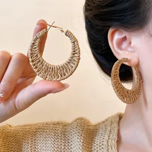 Bohemian style woven rattan hoop earrings with gold metal accents worn by a model