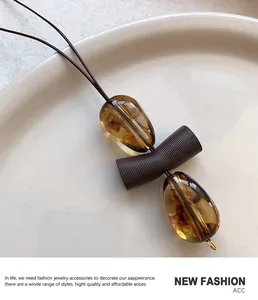 Detail view of the amber resin teardrop pendant with a textured brown bead and rope cord