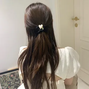 Detail of black fabric scrunchie with cream heart charm on elegant model hairstyle