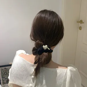 Detail of heart-shaped charm on elegant black velvet elastic scrunchie for low ponytail