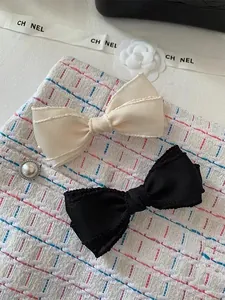 Detailed view of cream and black bow hair clips with elegant wavy scalloped edges