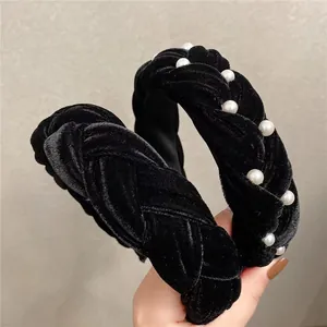 Detail of a thick black velvet braided headband with white pearl accents on soft fabric