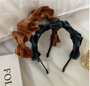 Elegant velvet bow headbands in dark green and caramel brown displayed on white fabric