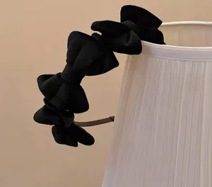 Detail of five velvet bows on a slim black headband styled on a pleated lamp