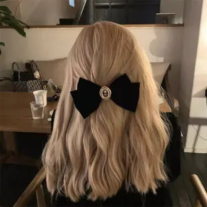 Barrette nœud en velours noir avec rose dorée et perles sur cheveux blonds ondulés