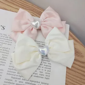 Detail showing satin pink and ivory bow hair clips with pearl heart accents on a desk