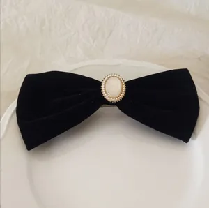 Close-up of black velvet bow hair clip with oval faux gemstone and small pearls