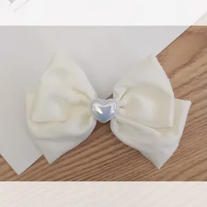 Close-up of cream bow hair clip featuring a pearlescent heart center on wood background