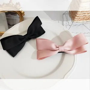 Elegant satin bow hair clips in pink and black on a white decorative ceramic plate