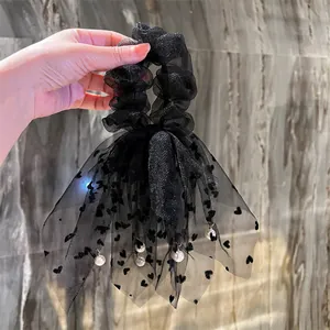 Dettaglio dell'elastico in mesh nero con cuori, fiocco e pendenti di perle bianche