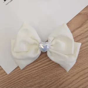 Cream satin bow hair clip with a pearl heart charm on a minimalist background