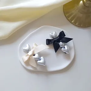 Elegant bow hair clips with three pearly hearts in black and cream on ceramic tray