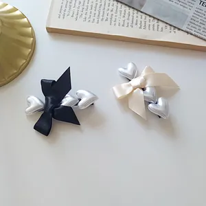 Close-up of elegant satin bow hair clips with silver metallic heart accents in black and beige
