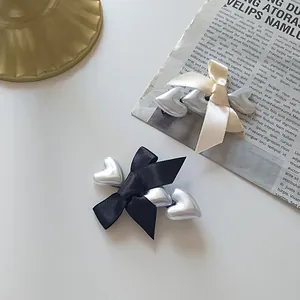 Close-up of black and beige satin bow hair clips with silver heart-shaped pearl details