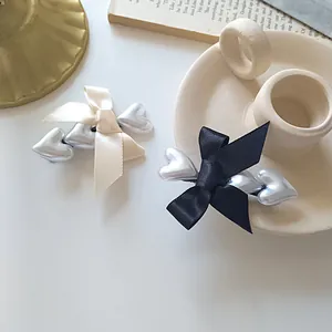 Elegant satin bow hair clips with metallic heart charms in cream and black tones