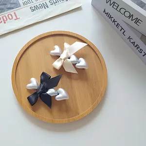 Detail of elegant satin bow hair clips with silver heart charms on a wooden tray