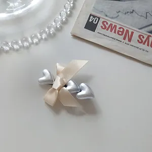 Detail of cream silk bow hair clip with three silver metallic hearts on a newspaper backdrop