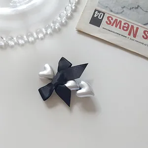 Detail of a black satin bow hair clip featuring three silver heart-shaped pendants