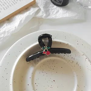 Detail einer schwarzen Haarklammer mit Strass-Kirschen-Anhänger auf einer Keramikplatte