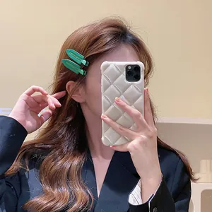 Détail d'une pince à cheveux verte en résine et d'une coque de téléphone matelassée