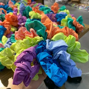 Hand holding vibrant multicolored fabric scrunchies with elastic pleated design details