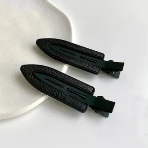 Détail de la texture cuir noir mat sur des pinces à cheveux géométriques au design épuré