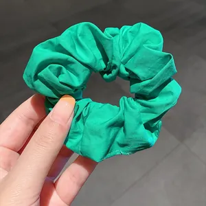Vibrant green fabric scrunchie with soft pleats shown from a top-down view on gray floor