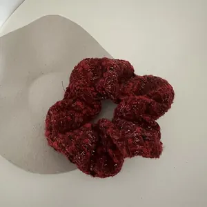 Detail of red tweed scrunchie with metallic fibers on grey stone accessory stand