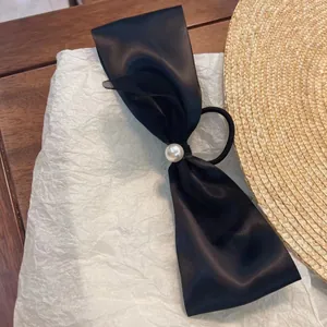 Detail of black satin bow hair tie with mesh overlay and center faux pearl decoration