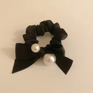 Elegant black satin scrunchie with layered bow and white pearls on beige surface