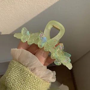 Pince à cheveux vert clair mat avec des papillons irisés tenue à la main par une femme
