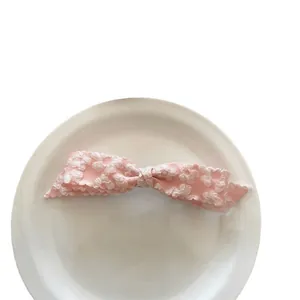 Pink ribbon bow hair clip with white floral embroidery presented on a white plate