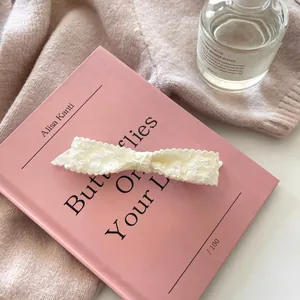 Close-up of off-white lace bow hair clip with floral embroidery on pink book background