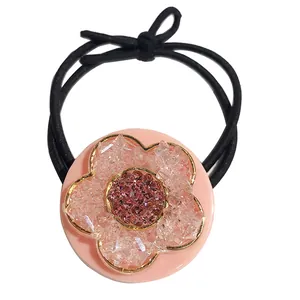 Elastic black hair tie with a pink resin flower ornament and gold metallic trim