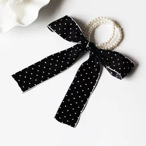 Detail of elegant black polka dot satin bow hair tie with luxury faux pearl elastic band