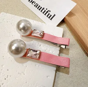 Detail shot of two pink ribbon hair clips with large pearls and faceted rhinestones