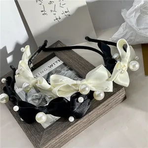 Detail view of elegant bow headbands with pearls in black and cream on a wooden frame