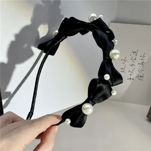 Detail of handmade black satin headband with bow design and elegant pearl accents