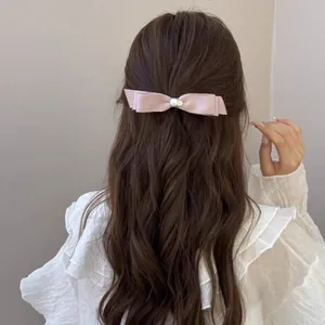 Barrette nœud en satin rose avec perle centrale sur de longs cheveux bruns ondulés