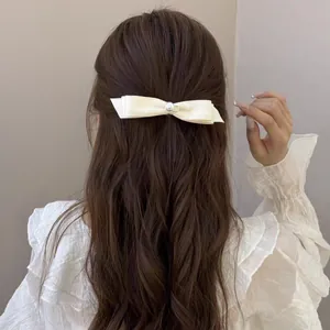Barrette nœud élégante couleur crème avec perle centrale sur cheveux ondulés