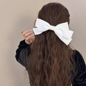 Elegant white satin multi-layered bow hair clip shown on long wavy hair from behind