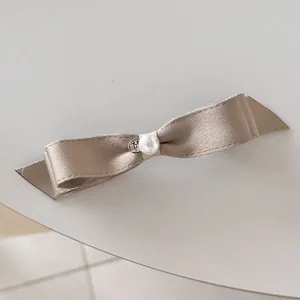 Détail d'un nœud papillon en satin champagne avec perle et breloque en forme de cœur