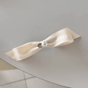Détail d'un nœud papillon en satin crème avec perle centrale et breloque argentée vintage