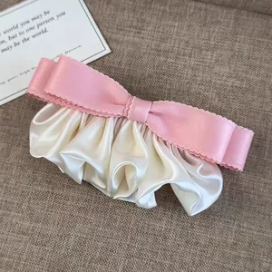 Détail d'une pince à cheveux à nœud rose avec plis en satin crème sur fond en lin texturé