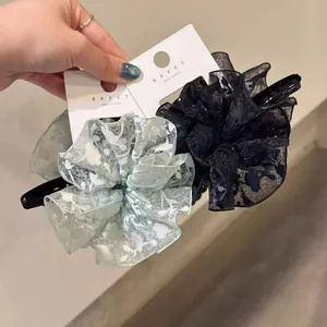 Pinces à cheveux en dentelle surdimensionnées vert clair et noir présentées à la main